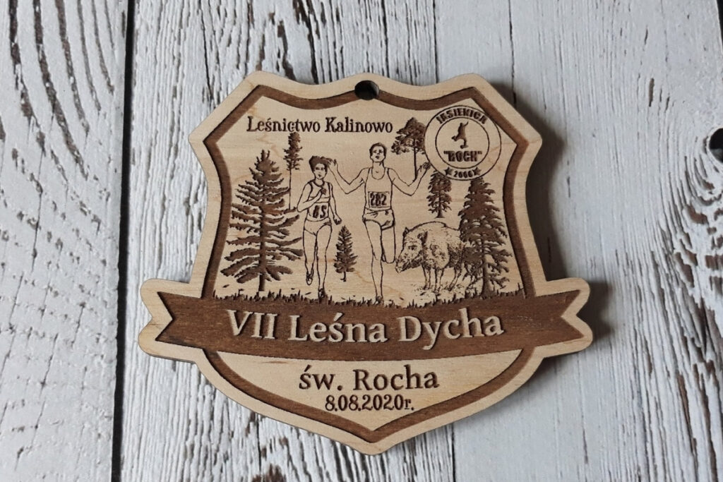 Drewniany medal na bieg „VII Dycha św. Rocha”, z precyzyjnym grawerem leśnych drzew, biegaczy, oraz logotypem wydarzenia, wykonany z naturalnie jasnej brzozy bez śladów dymu i osmaleń.
