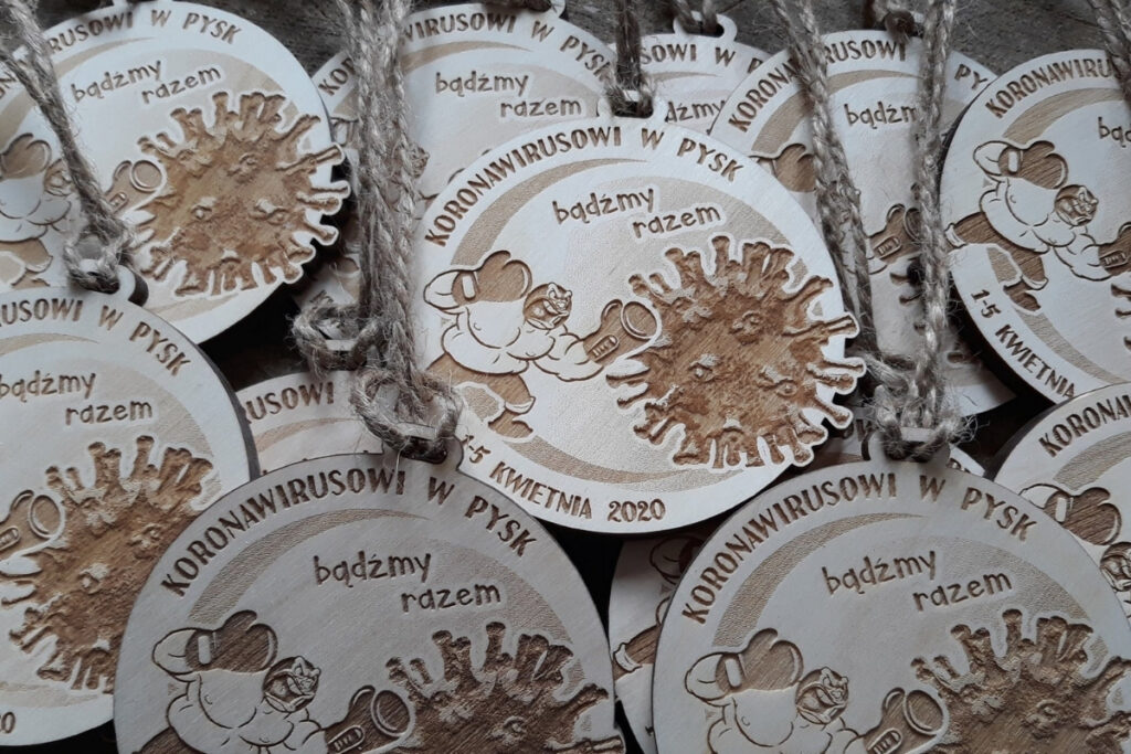 
Okrągły drewniany medal z grawerem cząsteczki wirusa z napisem „Koronawirusowi w pysk!”, upamiętniający sportową wytrwałość w dobie pandemii, wykonany z czystej brzozy bez śladów osmaleń.
