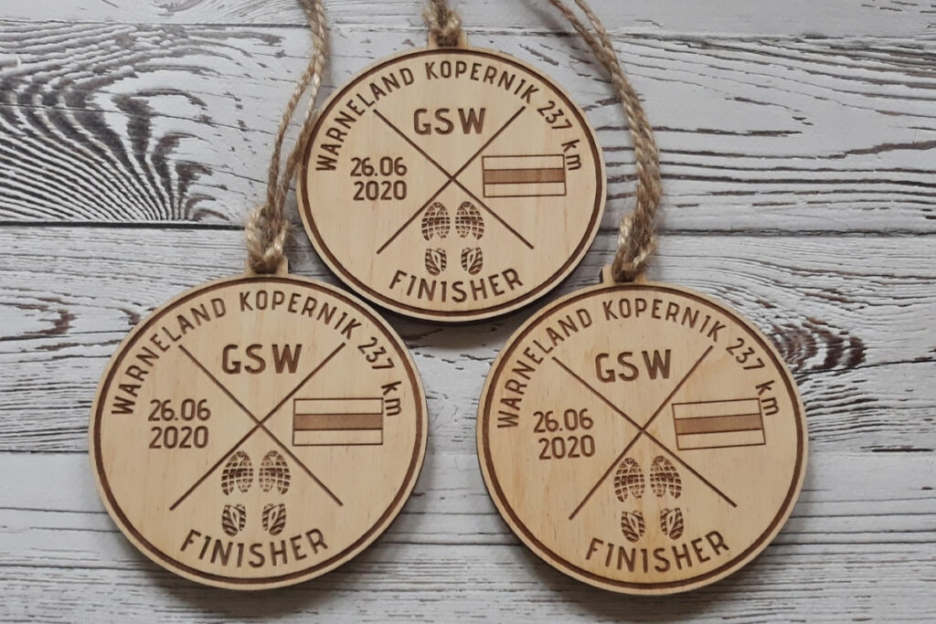 Tekst alternatywny (Alt Text):
Okrągły drewniany medal dla zwycięzcy ekstremalnego biegu „Warneland Kopernik 237 km”