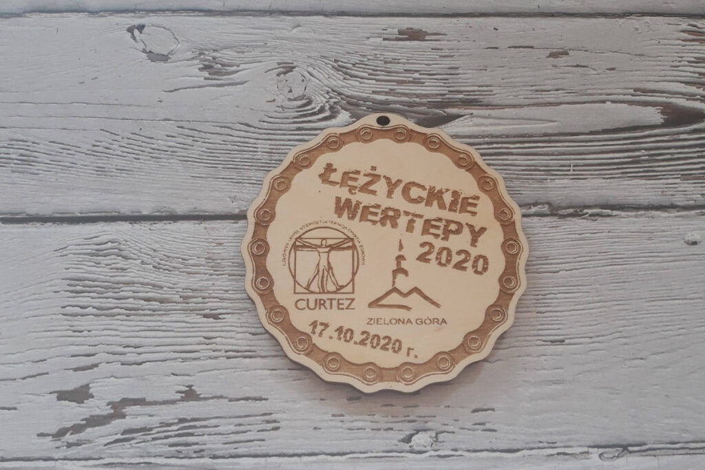 Okrągły drewniany medal na rajd rowerowy „Łużyckie Wertepy”, logotypów, nazwy i ramką z wygrawerowanego łańcucha rowerowego.