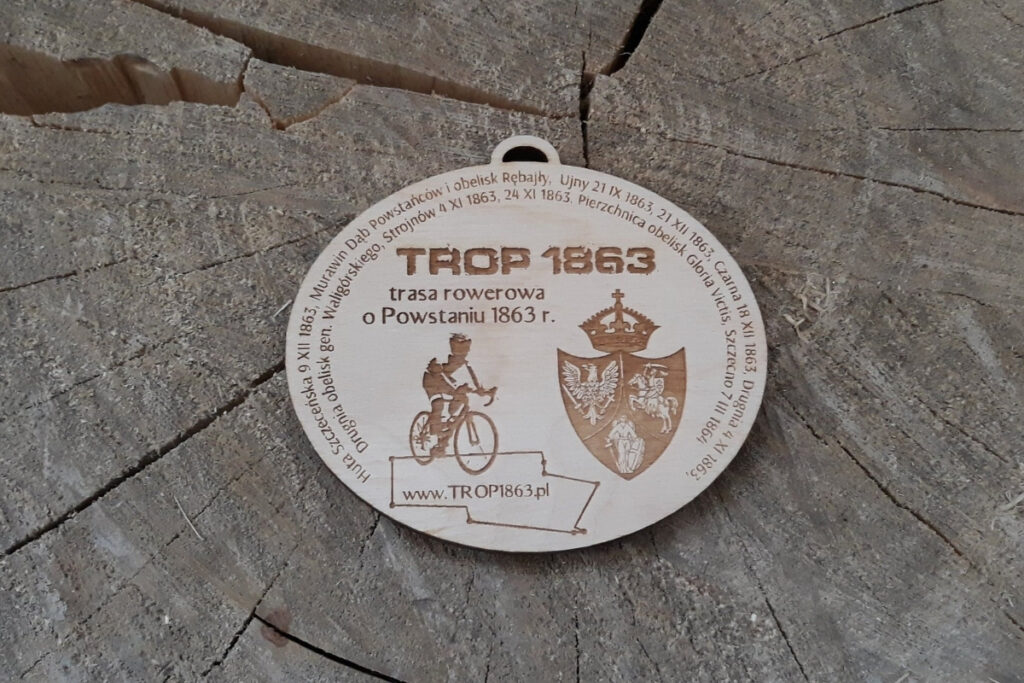 Owalny drewniany medal na rajd rowerowy z motywem historycznym, przedstawiający grawer postaci rowerzysty oraz pamiątkową inskrypcję, wykonany z czystej brzozy bez osmaleń.