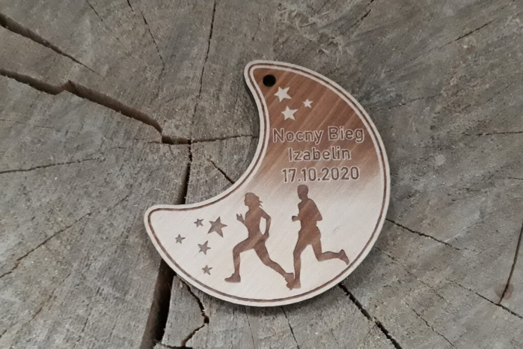 Drewniany medal w kształcie półksiężyca na „Nocny Bieg”, z grawerem rozgwieżdżonego nieba, sylwetką biegacza oraz nazwą wydarzenia, wykonany z jasnej brzozy bez śladów dymu i osmaleń.
