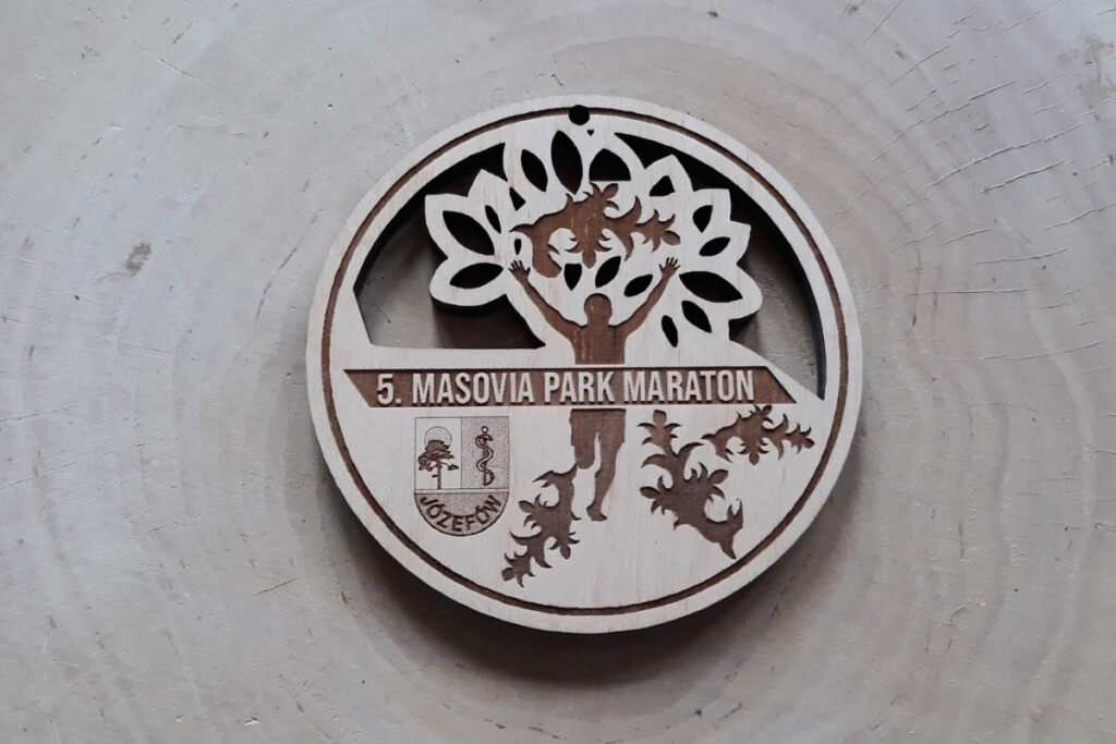 Ażurowy drewniany medal na „Masovia Park Maraton”, z precyzyjnie ażurowo wyciętymi motywami liści dębu, sylwetką biegacza z rękami w górze oraz herbem, wykonany z czystej płyty brzozy bez śladów dymu i osmaleń.