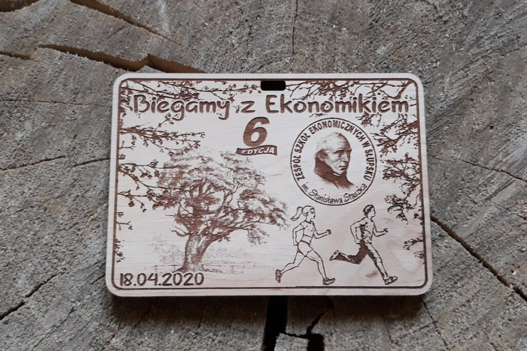 Prostokątny drewniany medal na „Bieg z Ekonomikiem”, z bogatym grawerem leśnych gałązek, biegaczami, oraz logotypem szkoły, wykonany z jasnej brzozy o czystych krawędziach bez osmaleń.