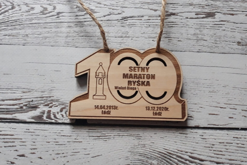 Drewniany medal jubileuszowy na „Setny Maraton Ryśka”. Medal w kształcie cyfry 100, wykonany z czystej brzozy bez śladów przypaleń.