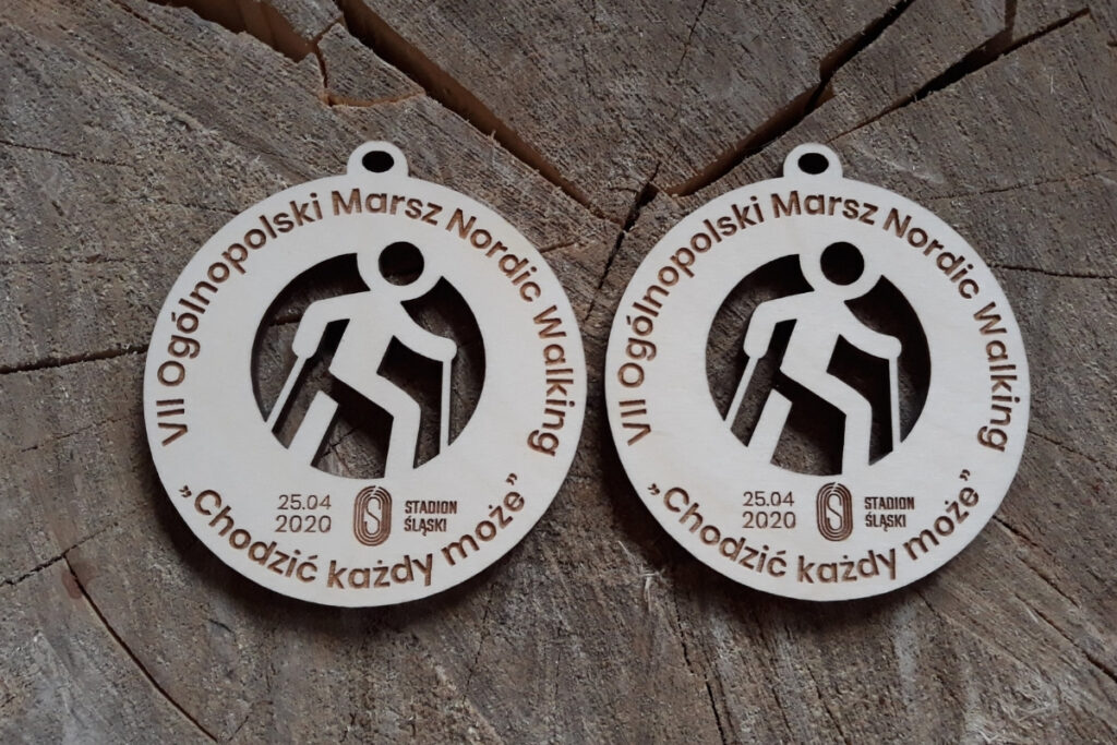 Okrągły drewniany medal na Ogólnopolski Rajd Nordic Walking „Chodzić każdy może”, z ażurowo wyciętą sylwetką osoby maszerującej z kijkami oraz grawerem logotypu wydarzenia, wykonany z czystej brzozy bez śladów dymu.