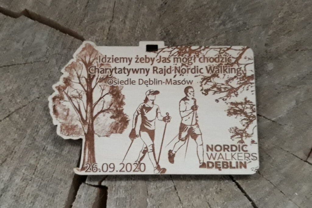 Prostokątny drewniany medal na Charytatywny Marsz Nordic Walking z grawerem pary maszerującej z kijkami,  oraz inspirującym cytatem o pomaganiu, wykonany z jasnej brzozy bez śladów dymu.