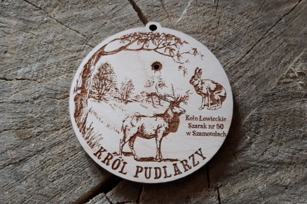 Drewniany medal na sklejce brzozy, przedstawiający grawer  jelenia byka oraz napis „Król Pudlarzy”, wykonany w rustykalnym, naturalnym stylu.