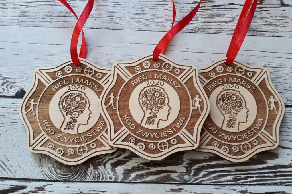 Nieregularnych kształtów drewniany medal z grawerem głowy z trybbami - nawiązującymi do nazwy - kod zwycięstwa, jakby kodem binarnym w tle oraz hasłem „Bieg i Masz kod Zwycięstwa”, wykonany z czystej płyty z brzozy o nieskazitelnie jasnej powierzchni bez osmaleń.