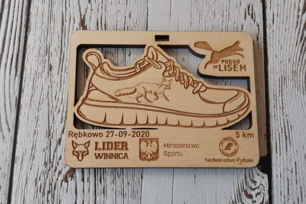 Prostokątny drewniany medal na bieg „Pogoń za lisem”, z precyzyjnie wyciętym ażurowym kształtem buta sportowego, grawerem uciekającego lisa oraz nazwą zawodów, wykonany z jasnej brzozy bez osmaleń.