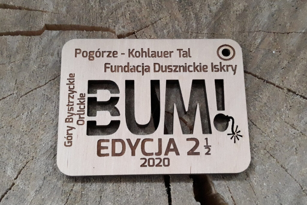 Prostokątny drewniany medal z grawerem stylizowanej, komiksowej bomby z zapalonym lontem i napisem wyciętym ażurowo „BUM”, wykonany z czystej brzozy bez śladów przypaleń i dymu.