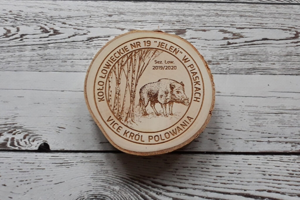 Naturalny drewniany medal na „Vice-Króla Polowania”, wykonany na autentycznym plastrze brzozy z korą o imponującej średnicy ok. 11 cm, z głębokim grawerem dzika odyńca oraz napisem okolicznościowym, zachowujący jasny odcień drewna bez osmaleń.