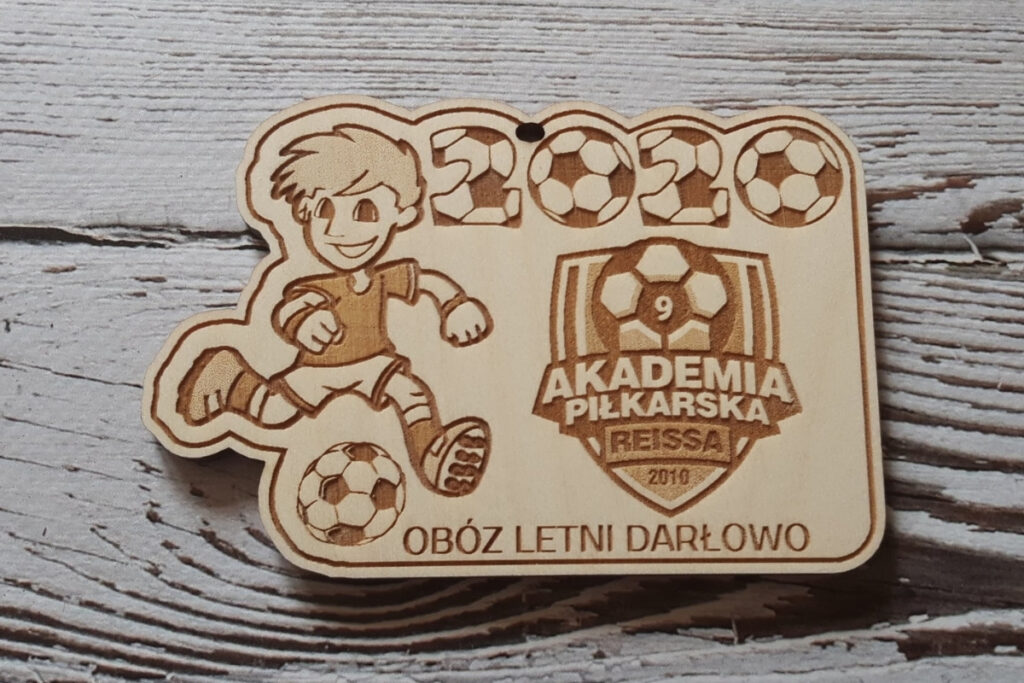 Drewniany medal z obozu piłkarskiego w Darłowie, z grawerem młodego piłkarza piłki nożnej oraz napisem „Obóz Letni Darłowo”, wykonany z jasnej brzozy bez osmaleń.