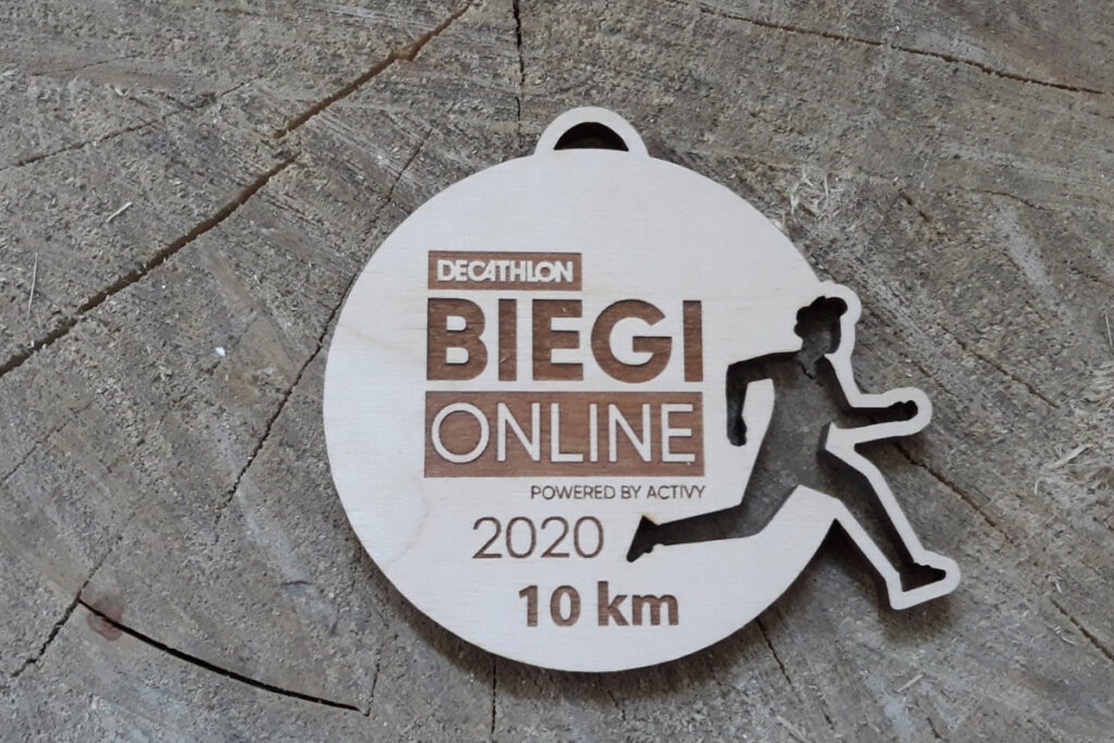 Ażurowy drewniany medal z wyciętą sylwetką biegacza, przygotowany na biegi online w formie ekologicznej pamiątki.