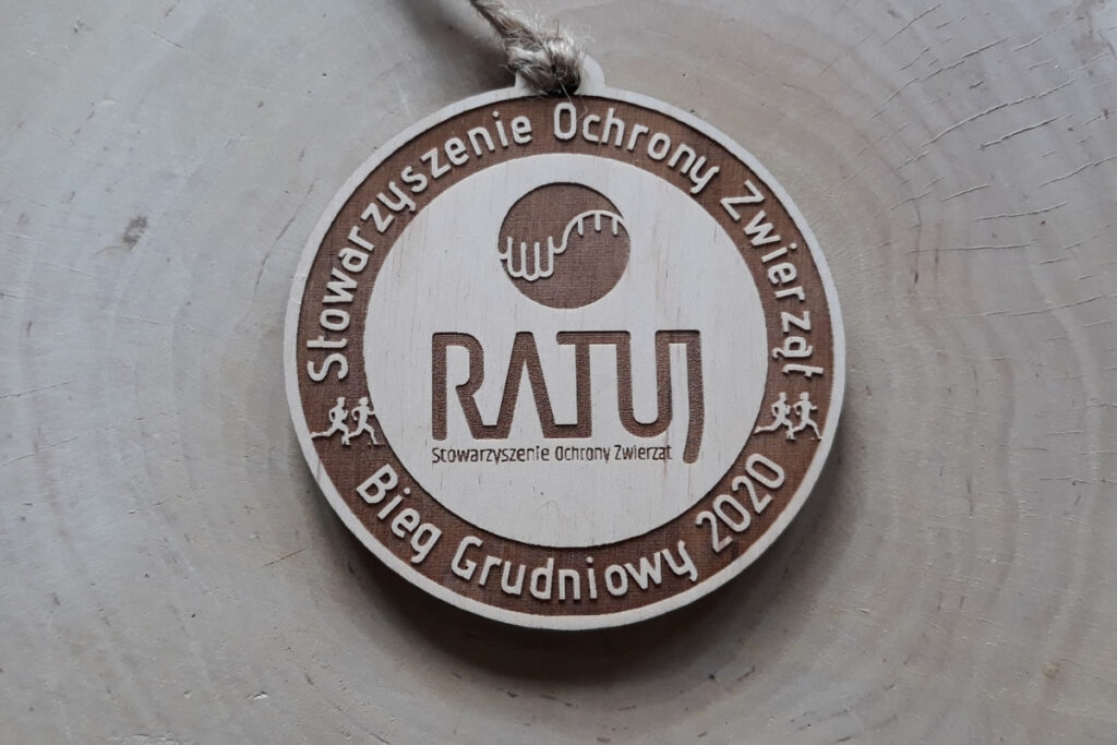 Okrągły drewniany medal dla Stowarzyszenia Ochrony Zwierząt „Ratuj”, z precyzyjnie wygrawerowanym logo stowarzyszenia w części centralnej, wykonany z jasnej brzozy o idealnie czystej powierzchni bez śladów osmaleń.
