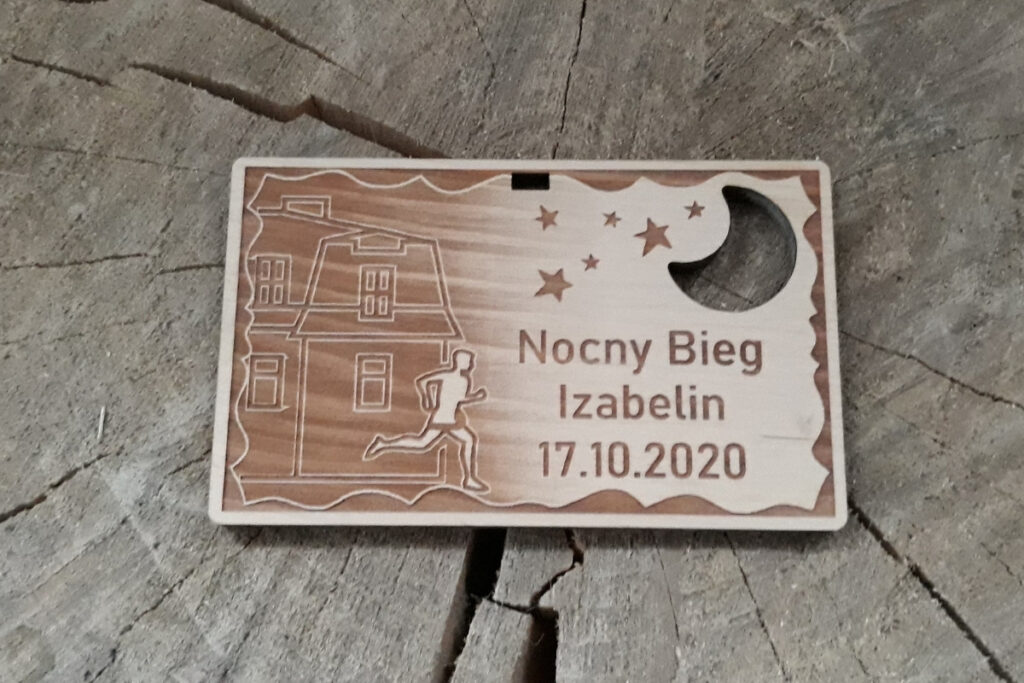 Prostokątny drewniany medal na Bieg Nocny w Izabelinie z grawerem sylwetki biegacza i ryciny zabudowy domów, oraz ażurowo wyciętym księżycu.