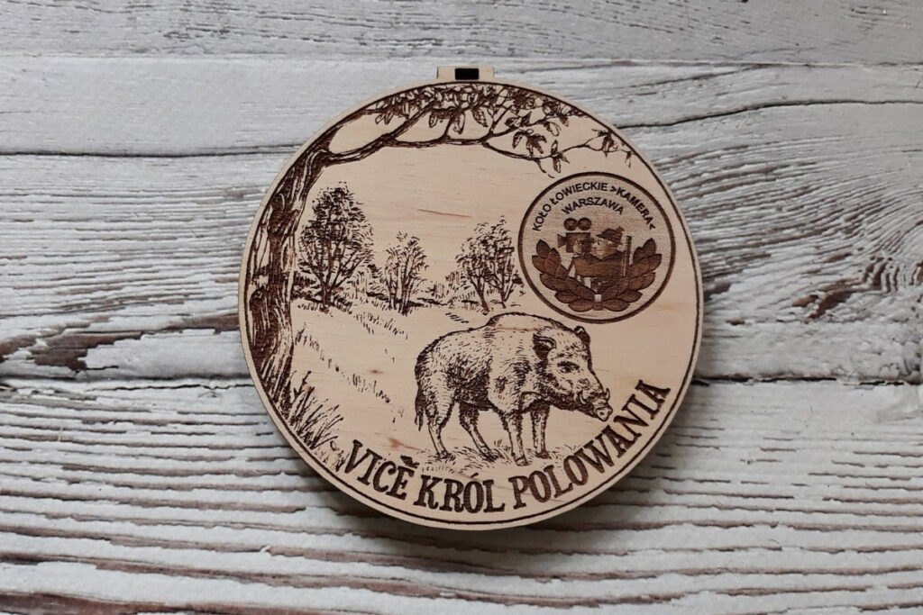 Okrągły drewniany medal dla Vice Króla polowania z precyzyjnym grawerem dzika na tle drzewa i krzewów.