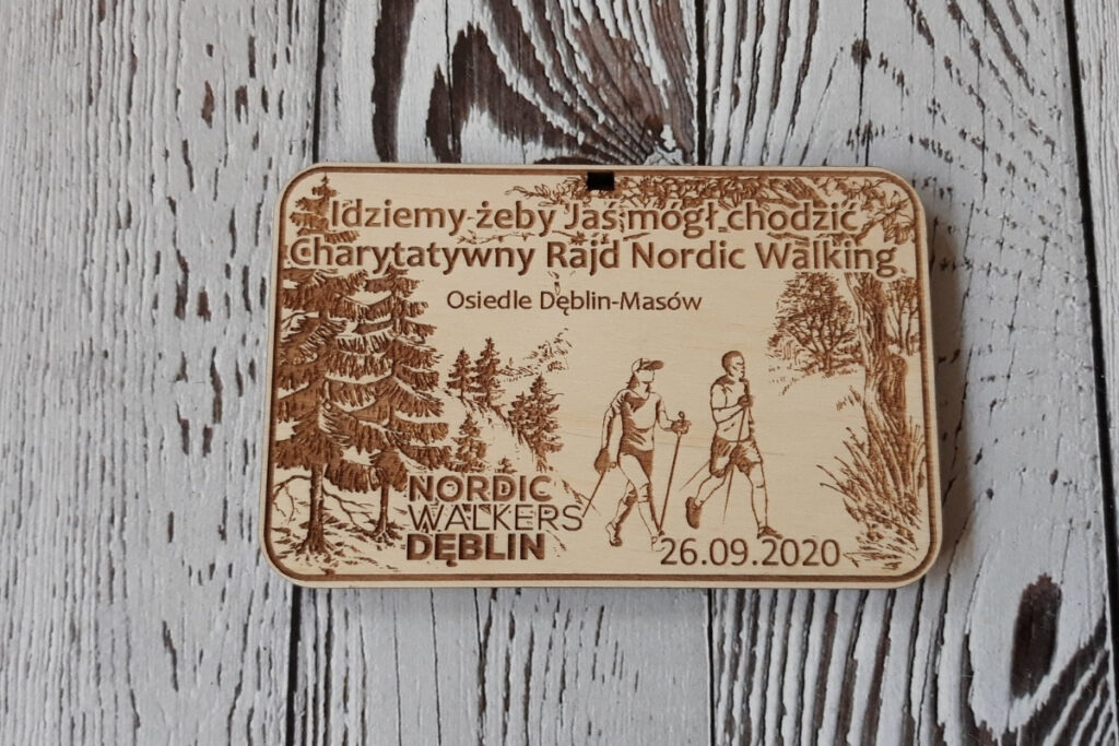 Prostokątny drewniany medal na Charytatywny Marsz Nordic Walking z grawerem pary maszerującej z kijkami,  oraz inspirującym cytatem o pomaganiu, wykonany z jasnej brzozy bez śladów dymu.