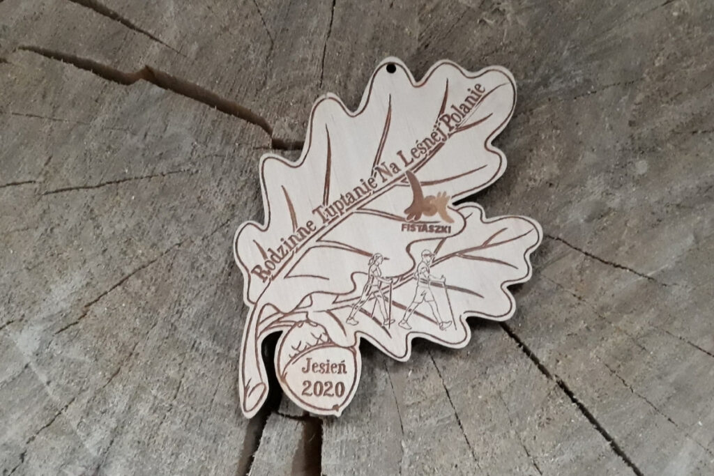Ekologiczny drewniany medal w kształcie liścia dębu z grawerowaną szyszką, przygotowany na wydarzenie Rodzinne Tuptanie.