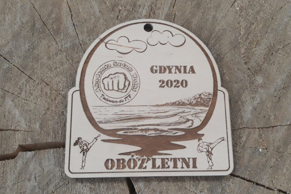 Półokrągły drewniany medal pamiątkowy z obozu letniego w Gdyni, z grawerem fal i brzegu,  wykonany z jasnej brzozy bez śladów osmaleń.