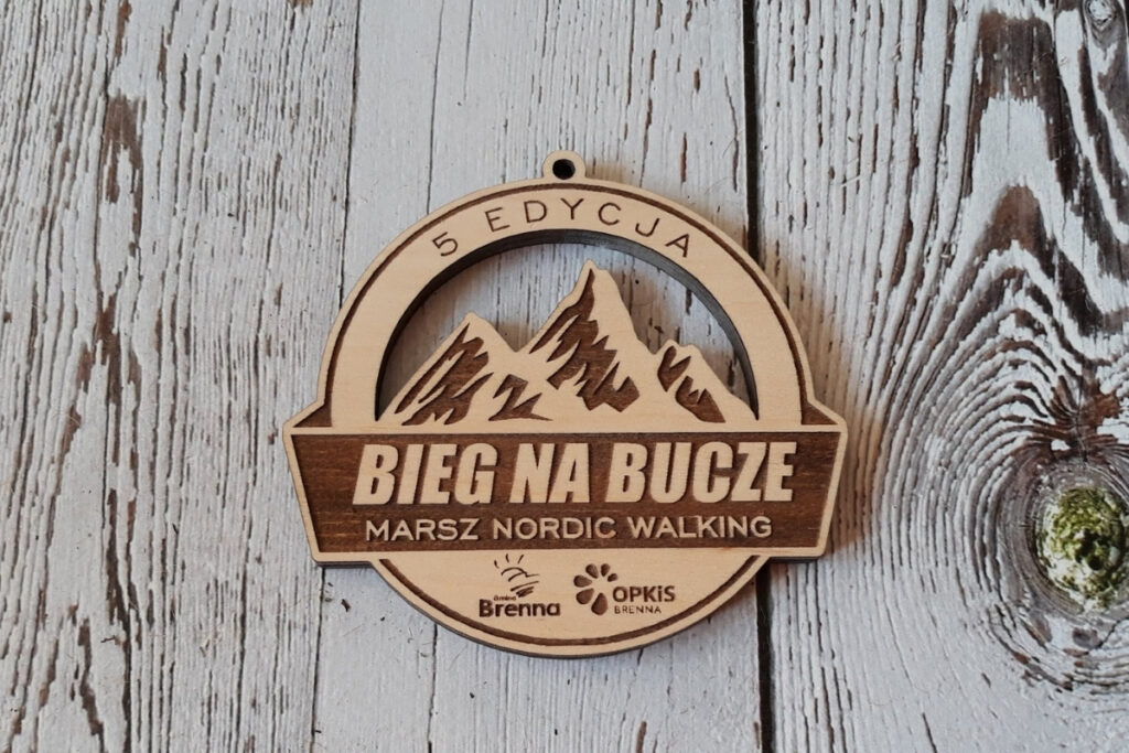 Ażurowy drewniany medal na Górski Bieg na Bucze z precyzyjnym grawerem górskiego szczytu i napisami Bieg na Bucze Marsz Nordic Walking oraz logotypami.