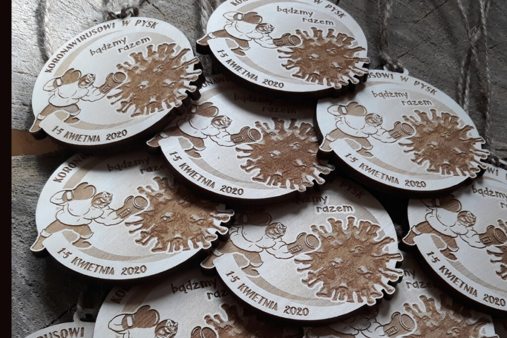 Okrągły drewniany medal z grawerem cząsteczki wirusa z napisem „Koronawirusowi w pysk!”, upamiętniający sportową wytrwałość w dobie pandemii, wykonany z czystej brzozy bez śladów osmaleń.