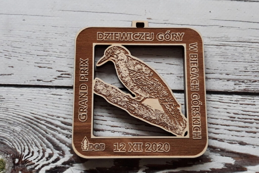 Prostokątny, ażurowy drewniany medal na Grand Prix Dziewiczej Góry z precyzyjnie wyciętym motywem ptaka.