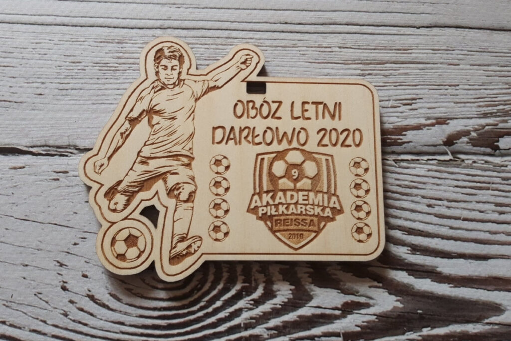 Drewniany medal na piłkarski obóz letni w Darłowie z grawerem zawodnika przy piłce i herbem klubu.