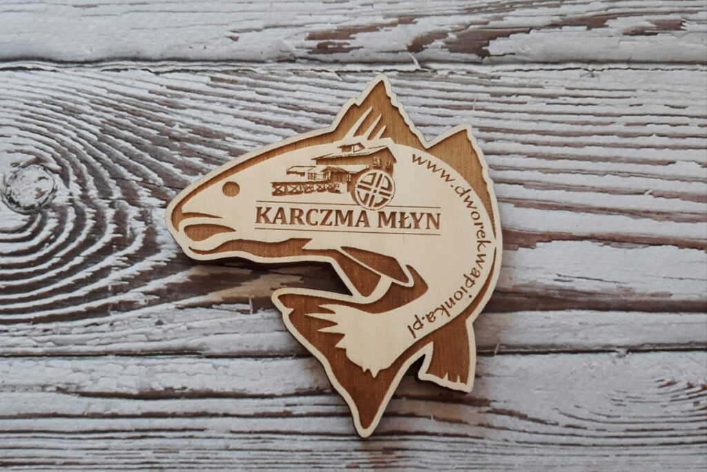Pamiątkowe drewniane magnesy w kształcie ryby z grawerowanym logo dla lokalnej karczmy.