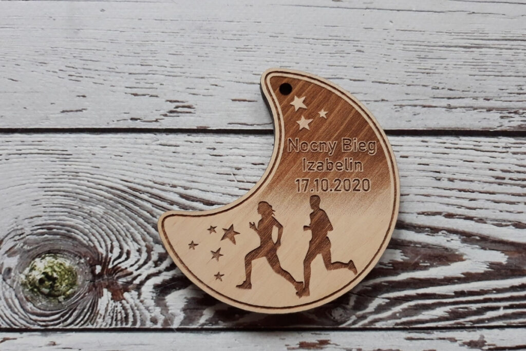 Wyjątkowy drewniany medal w kształcie półksiężyca na Nocny Bieg w Izabelinie z grawerem gwiazd i biegaczami..