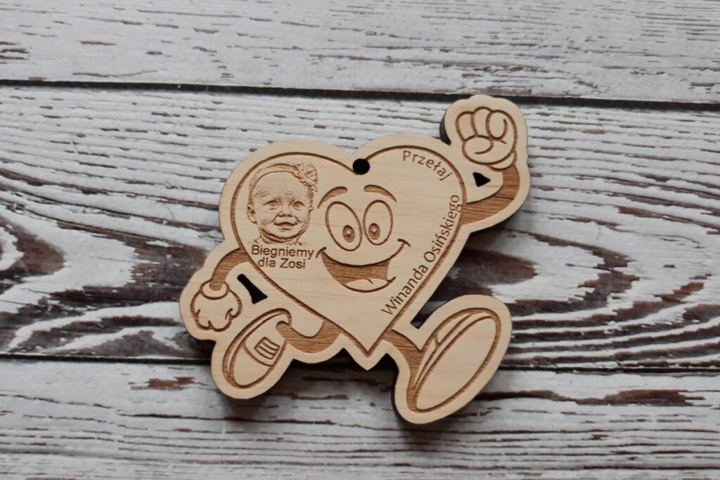 Drewniany medal charytatywny w kształcie biegnącego serca z rękami i nogami w ruchu.