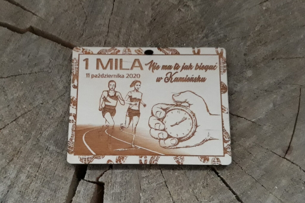 Nowoczesny prostokątny drewniany medal na bieg lekkoatletyczny na 1 milę z grawerem bieżni i sylwetki biegaczy, oraz ręką trzymającą stoper.