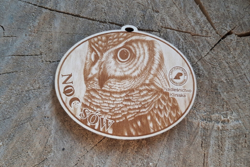 Okrągły drewniany medal na wydarzenie „Noc Sów” z bardzo szczegółowym grawerem portretu sowy.