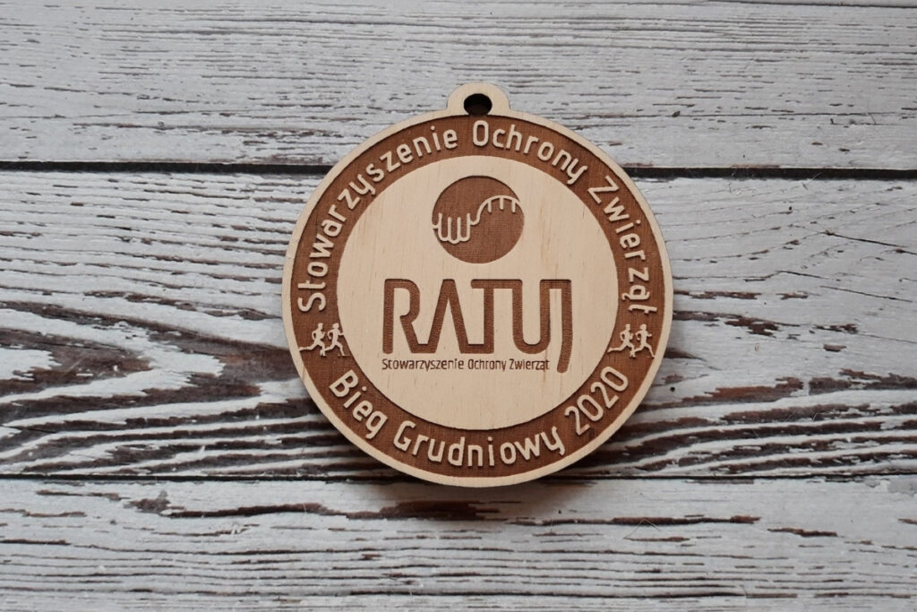 Okrągły drewniany medal dla Stowarzyszenia Ochrony Zwierząt z centralnie wygrawerowanym logotypem i napisami dookoła medalu.