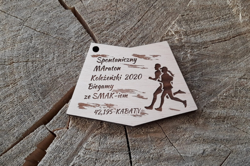 Drewniany medal na Maraton Koleżeński z grawerem napisów, sylwetką biegaczy i pamiątkową datą.