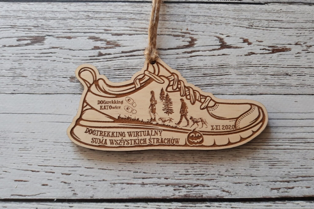 Drewniany medal w kształcie buta trekkingowego z grawerem spacerowiczów z psem, przygotowany na wirtualne zawody dogtrekkingu.