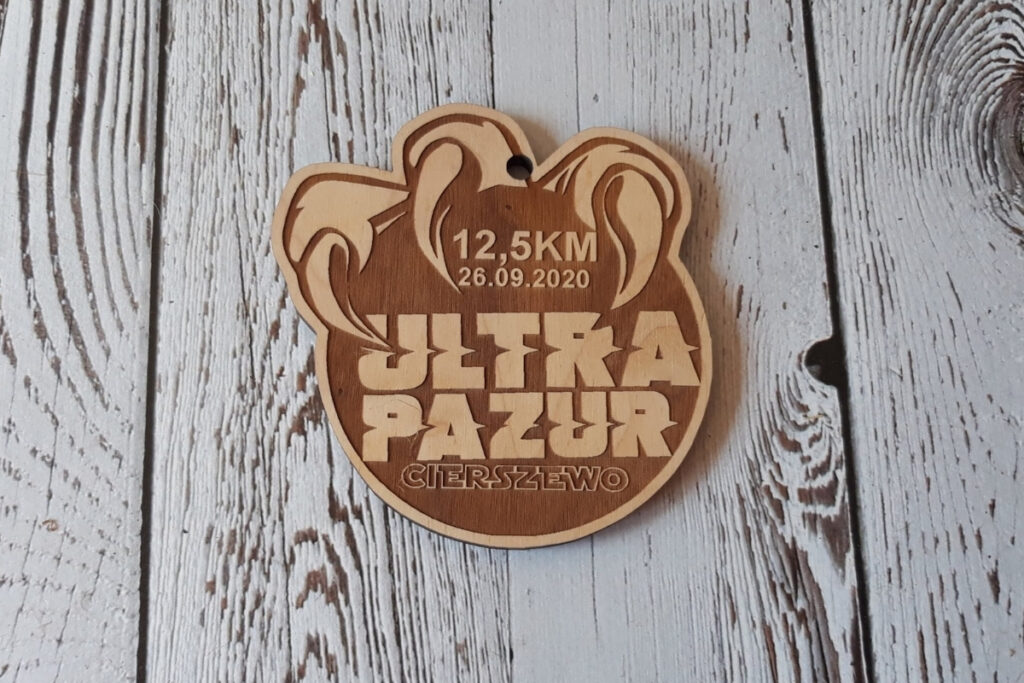 Unikalny drewniany medal wycięty w kształcie logotypu biegu Ultra Pazur, przedstawiający dynamiczny motyw pazura z precyzyjnym grawerem.